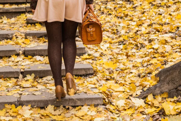 Women\'s feet are on the stairs in the park with golden autumn le