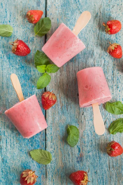 Strawberry sorbet with mint on a stick on a wooden table