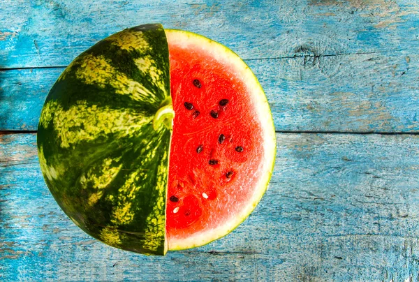 Watermelon with cut a piece of wood lying on a blue rustic backg