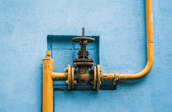 Yellow gas pipe with a valve on the blue wall