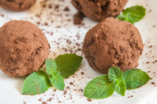 Dessert truffles sprinkled with cocoa and mint on white plate