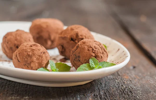 Dessert truffles sprinkled with cocoa and mint on white plate