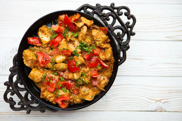 Chicken with vegetable on frying pan on white wood background