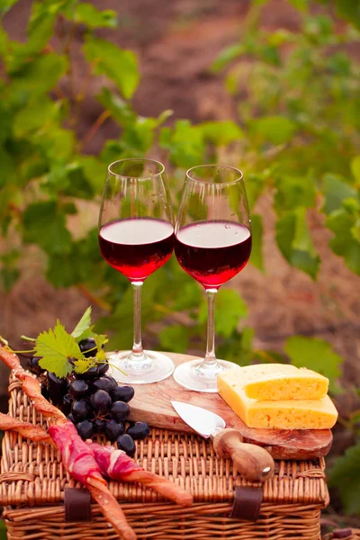 Two glasses of red wine with bread, meat, grape and cheese on th