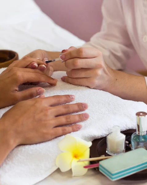 Woman in nail salon receiving manicure by beautician