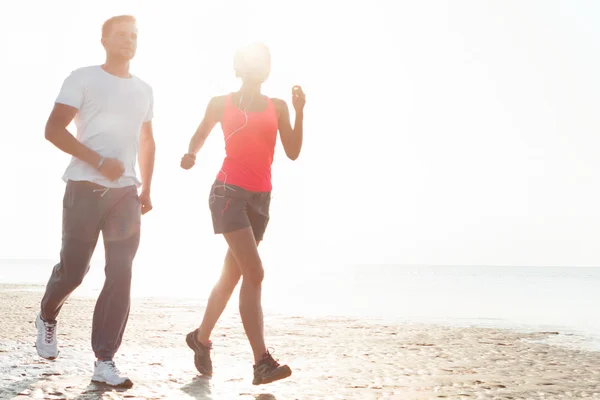 Young couple running together beside the water at the beach. Man