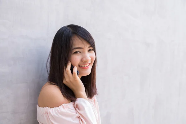 Beautiful asian young woman talking on Mobile Phone, over concrete wall