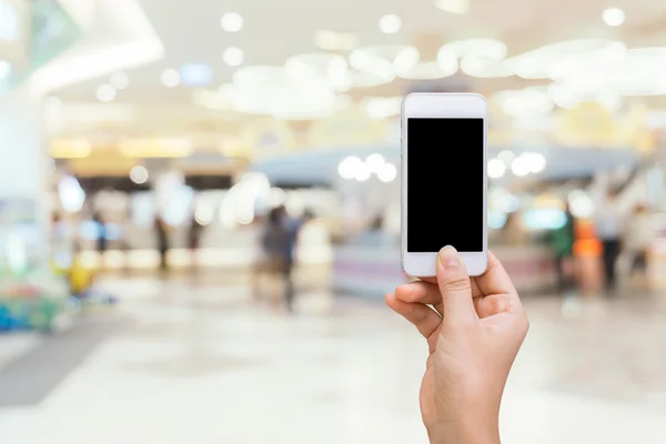 Smart phone with white screen in hand on blurred in shopping mall background,shopping online concept,shopping by smart phone