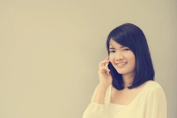 Beautiful asian young woman talking on Mobile Phone over concrete wall, vintage filtered image.