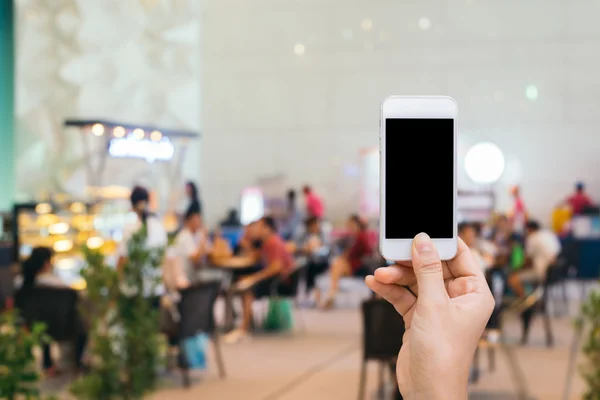 Smart phone with white screen in hand on blurred in shopping mall background,shopping online concept,shopping by smart phone