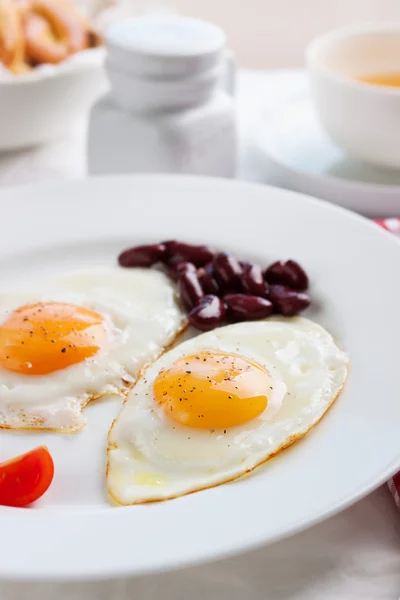 Homemade fried eggs with tomatoes and red kidney beans on a plate on a table with kitchen background, closeup