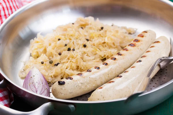 White grilled sausages with sauerkraut or cabbage, black pepper and fresh cold beer in a vintage pan on an old vintage green wooden background, closeup