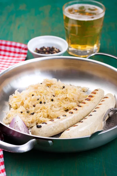 White grilled sausages with sauerkraut or cabbage, black pepper and fresh cold beer in a vintage pan on an old vintage green wooden background, closeup