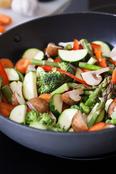Wok stir fry vegetables with zucchini, spring asparagus, paprika, carrot and broccoli, closeup in a wok pan in a kitchen