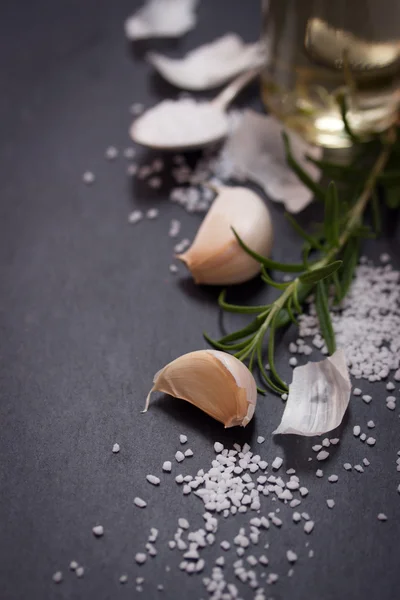 Garlic, rosemary, salt and olive oil on black stone background