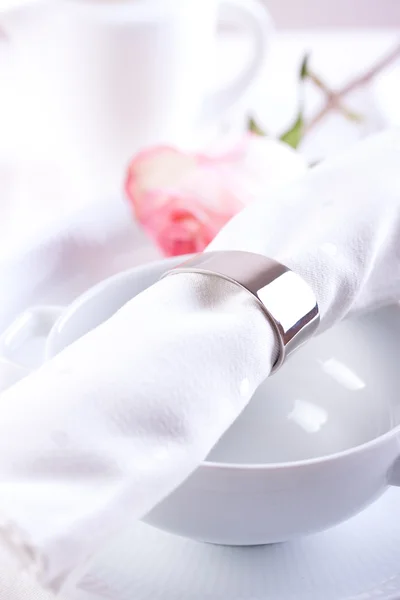White textile napkin with ring on white ceramic bowl with rose on background