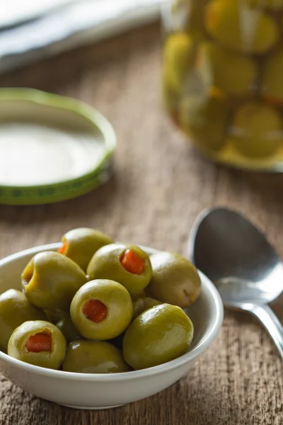 Green olives stuffed with red paprika in bowl on table.