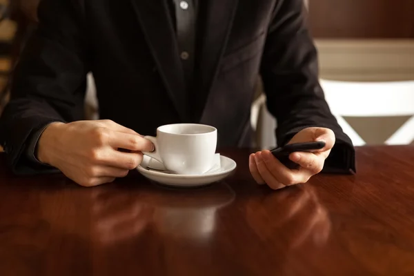 Man in a cafe drinking coffee and using a mobile phone.