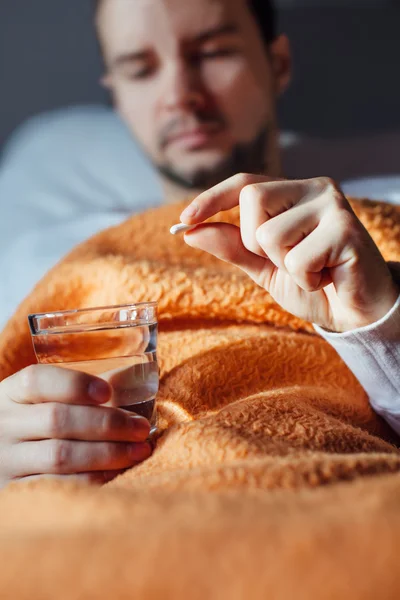 Sick man laying in bed under blanket and holding glass of water
