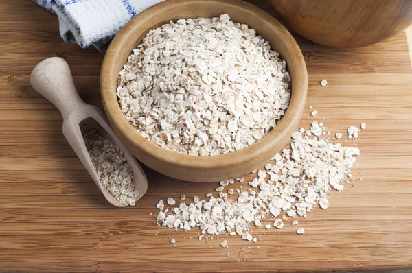 Oatmeal or oat flakes in bowl and scoop on dark wooden table