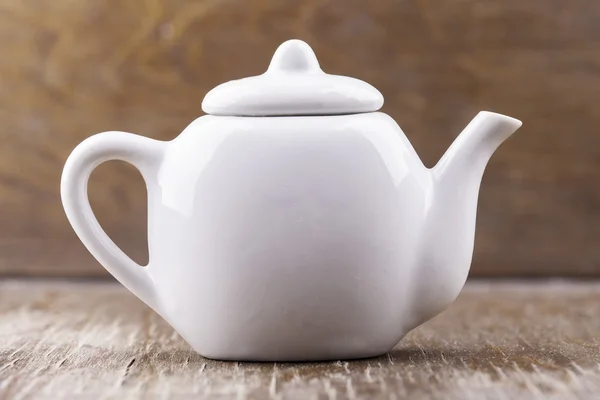 Small white ceramic teapot on a wooden surface closeup