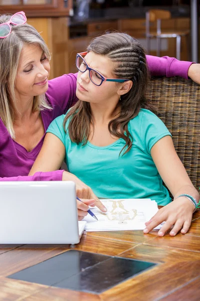 Pretty teen girl doing homework with a middle age mother