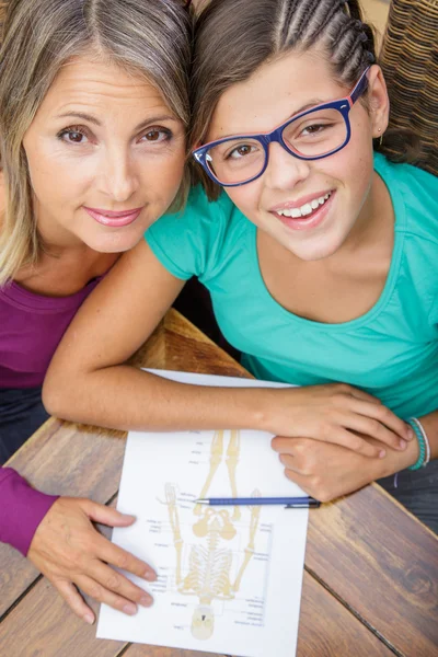 Smiling teen girl doing its homework with middle age teacher
