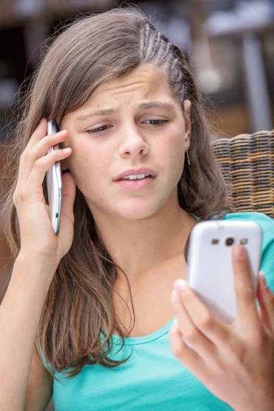 Closeup of a pretty young girl having a phone conversation with 2 phones
