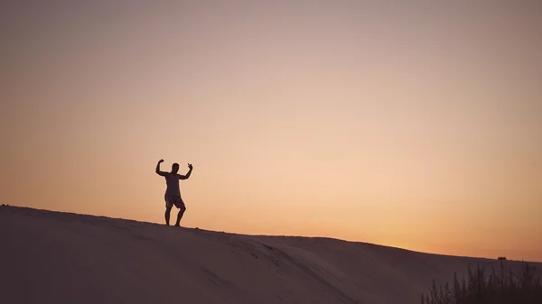 A guy standint on a top of sand-dune in the sunset light