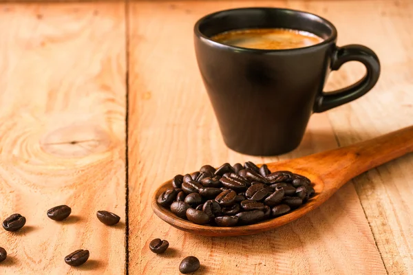 Coffee beans on wooden spoon with cup of espresso.