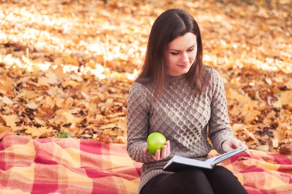 Woman with book and apple sitting on a rug