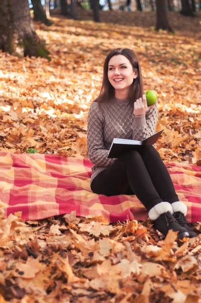 Woman with book and apple sitting on a rug