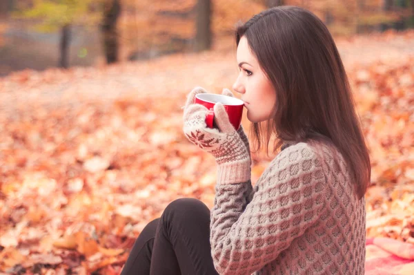 Young woman sitting in a park and drinking tea