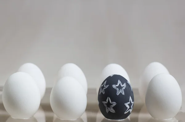 One black egg with a pattern among several white eggs