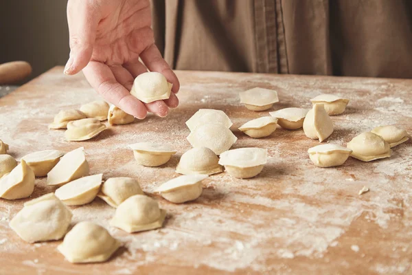 Woman hand holds one ravioli above others on wooden boards