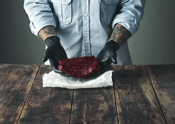 Tattooed butcher offers piece of meat on camera
