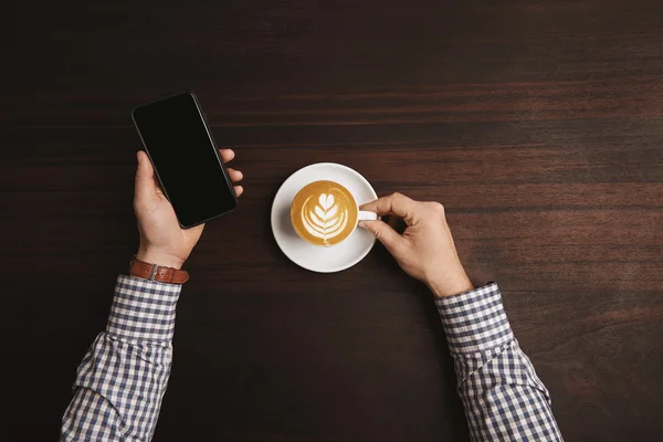 Top view accountant hands hold phablet and cup with cappuccino