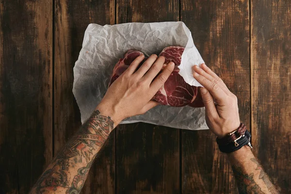 Hands folds three fresh raw meat steaks  in white craft paper