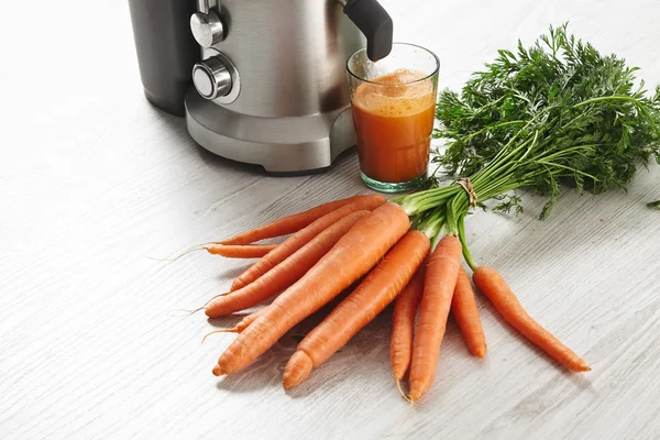 Metallic professional juicer with glass of carrot juice
