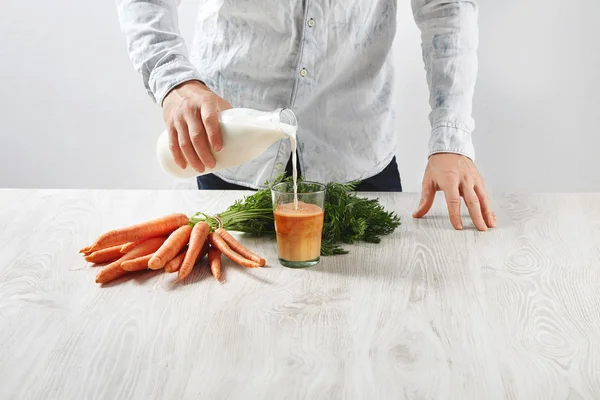 Man pours milk to glass with carrot juice