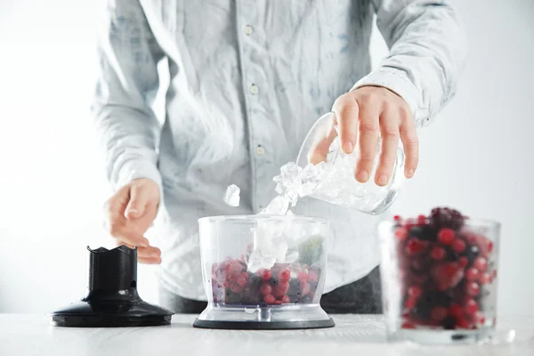 Man adds ice cubes to blender pot making smoothie