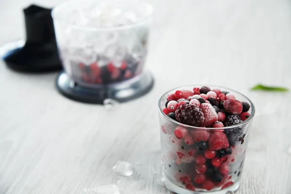 Blender pot with frozen berries and ice cubes