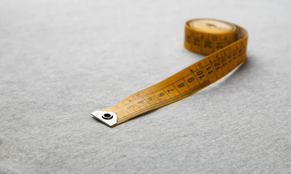Yellow measuring tape on gray fabric