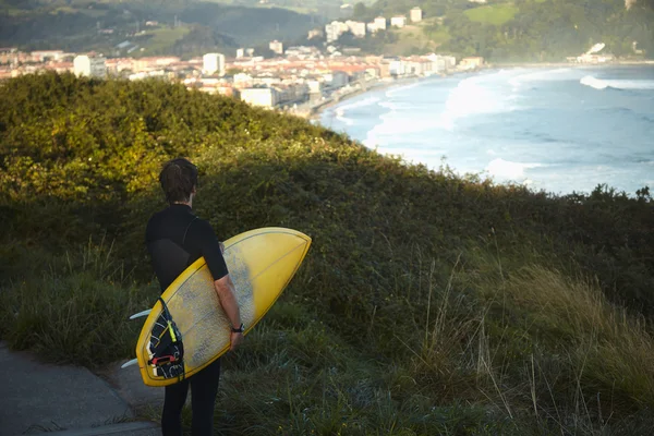 Surfer in wetsuit holds his surfboard