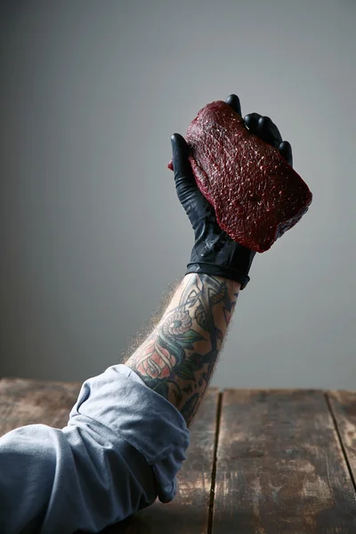 Tattooed left hand black silicon glove holds fresh whale meat steak