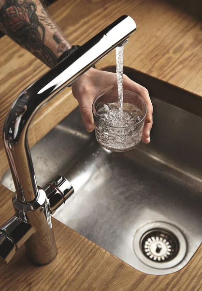 Tattooed hand fills glass with water from tap