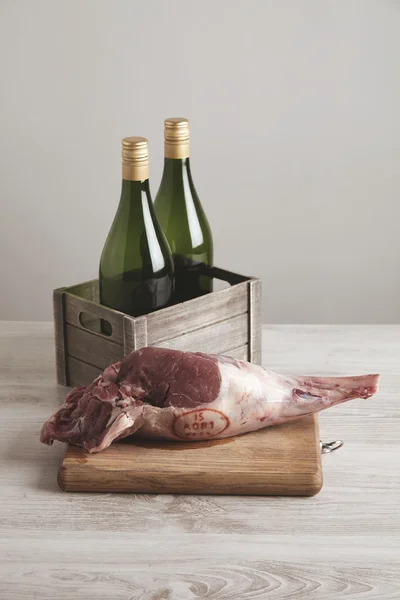 Raw lamb leg and two bottles in wooden box isolated