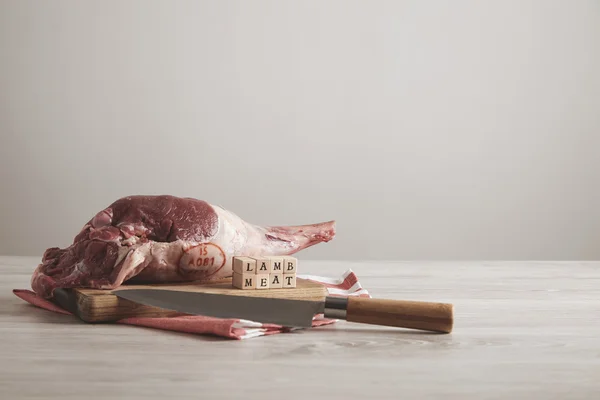 Raw meat lamb leg with letters on white table with knife