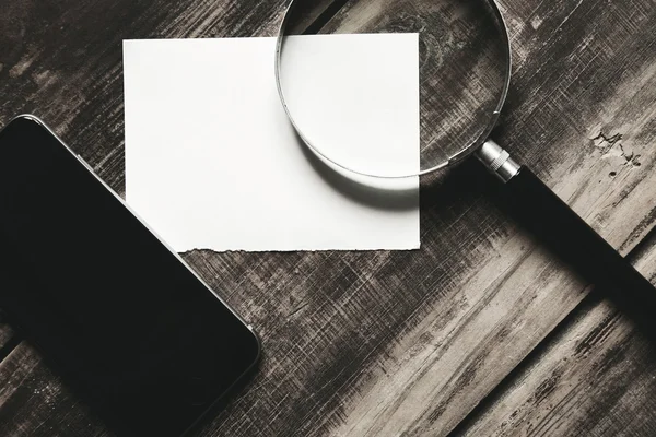 Side view smartphone, magnifier and paper on black table