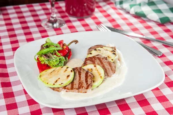 Restaurant served veal medallions with  with grilled vegetables and cheese sauce